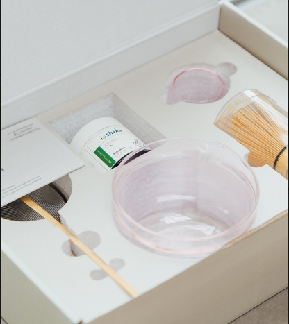 Pink Hario glass bowl, isshiki matcha tin, and bamboo whisk nestled in the set's white gift box