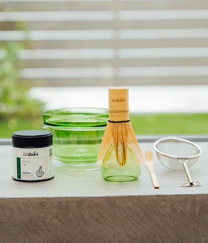 Green Hario glass bowl with bamboo whisk, Isshiki Samidori tin and strainer arranged on a stone ledge by a sunny window