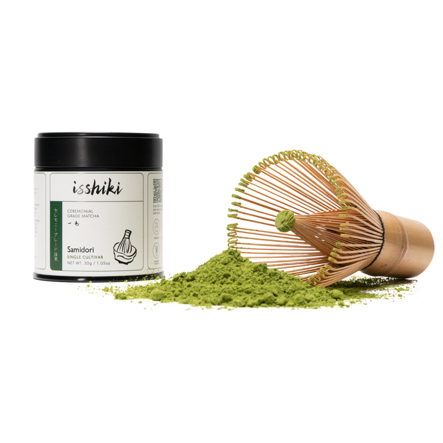 Isshiki Samidori ceremonial matcha tin beside a bamboo whisk resting on a mound of green matcha powder