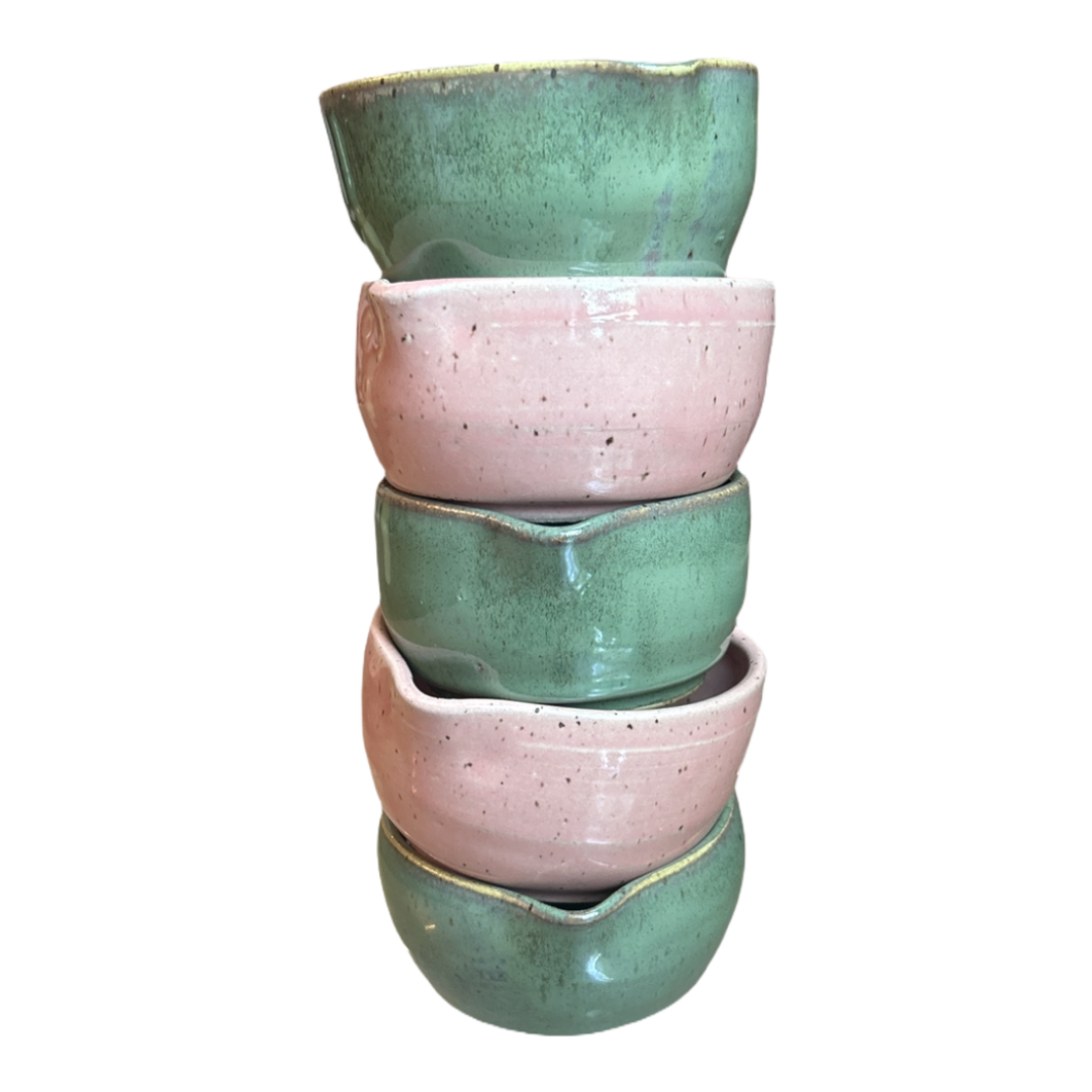 Five handcrafted heart-shaped matcha bowls in speckled green and pink glazes stacked in a tower