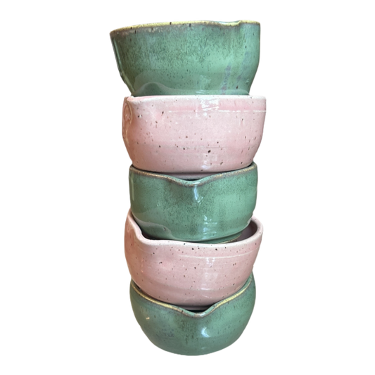 Five handcrafted heart-shaped matcha bowls in speckled green and pink glazes stacked in a tower