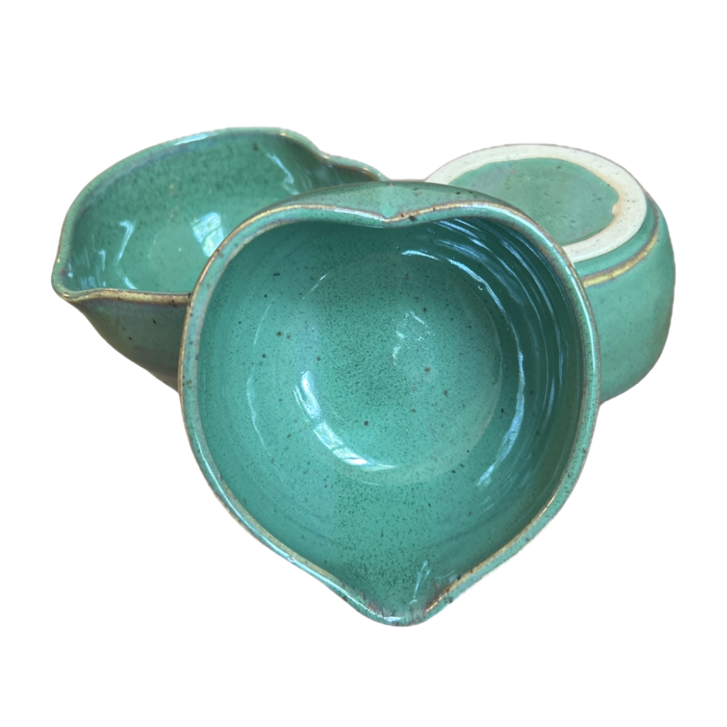 Three green heart-shaped matcha bowls grouped together, one tipped to show its interior