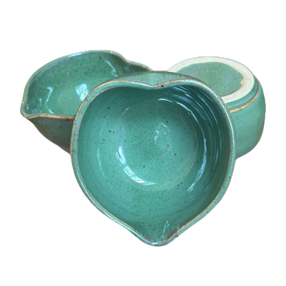 Three green heart-shaped matcha bowls grouped together, one tipped to show its interior