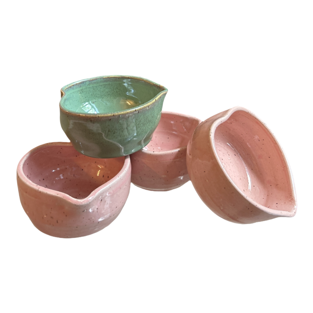 Four handcrafted heart-shaped matcha bowls, one speckled green and three pink, clustered together