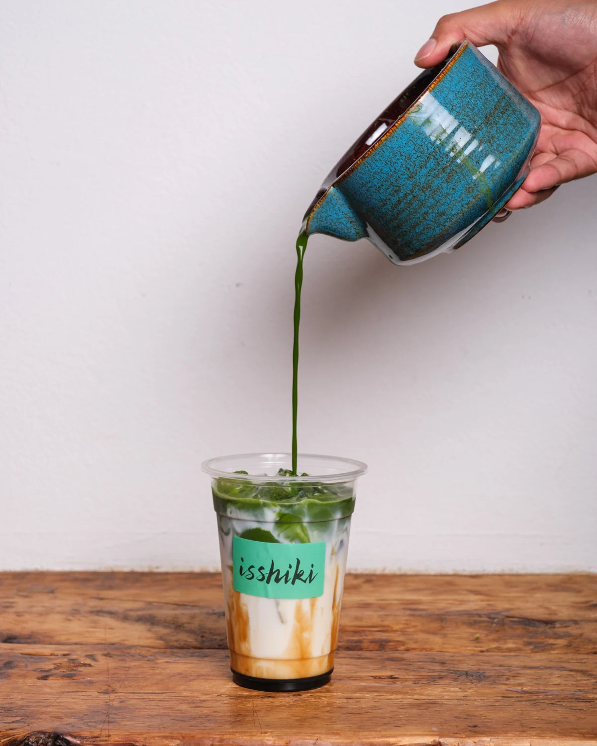 Matcha poured from a blue bowl into a clear Isshiki cup.